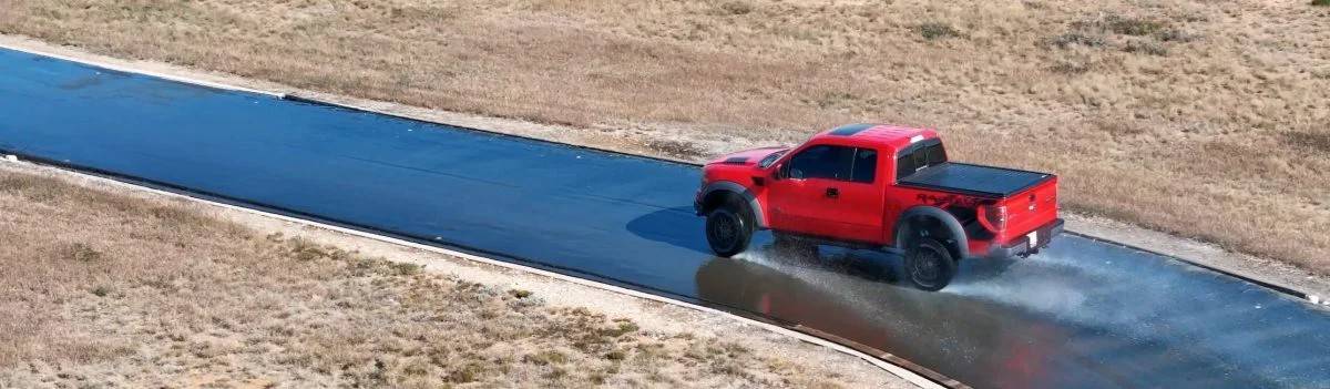 Красный пикап Ford Raptor выполняет скоростной заезд по треку во время тестирования управляемости на залитом водой покрытия полигона